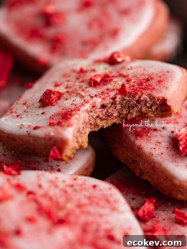 Strawberry shortbread cookies topped with glaze and freeze-dried strawberry bits randomly placed in a vintage baking tin.