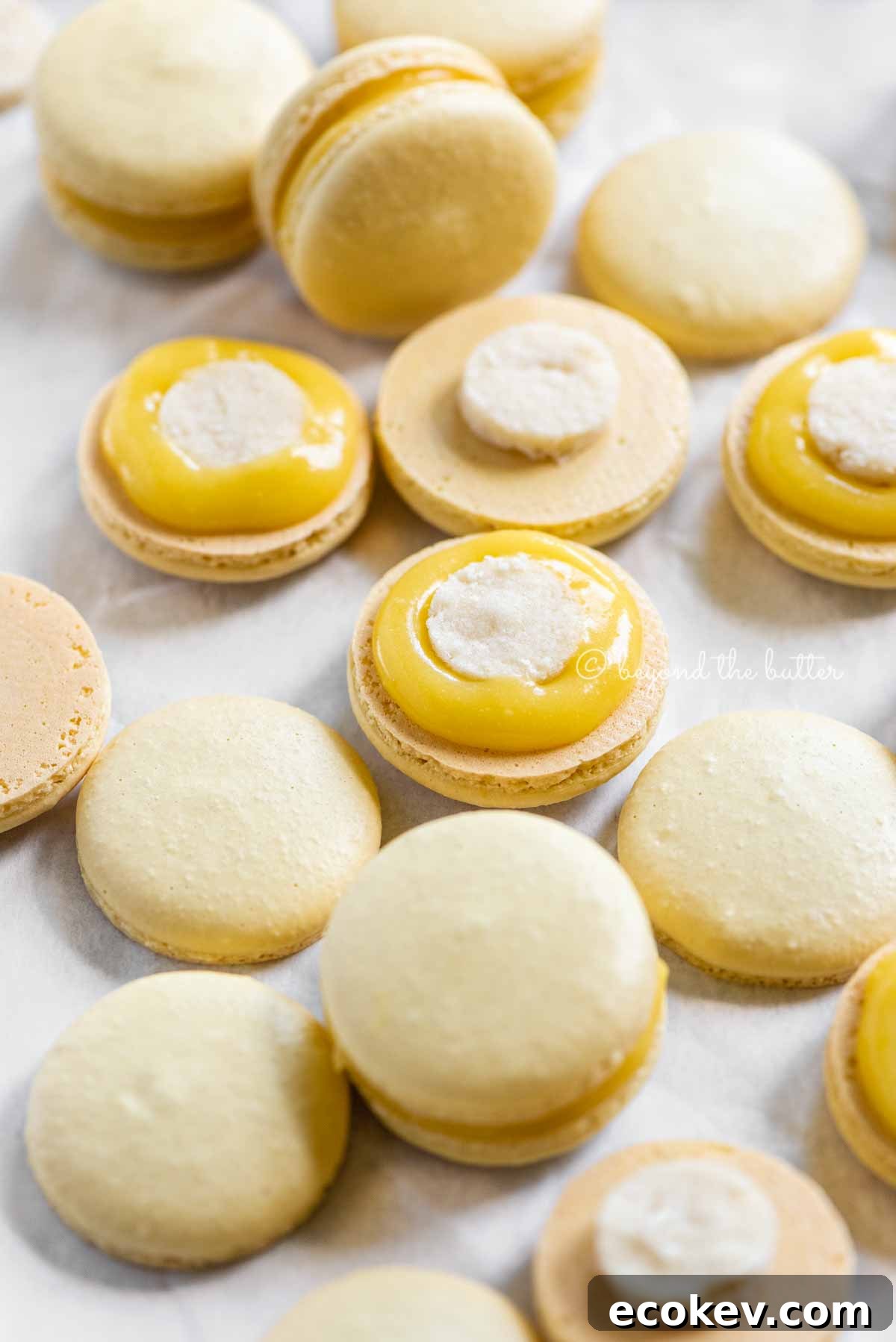 Angled image of lemon bar macarons half opened topped with shortbread crust centers and lemon curd filling | All Images © Beyond the Butter™