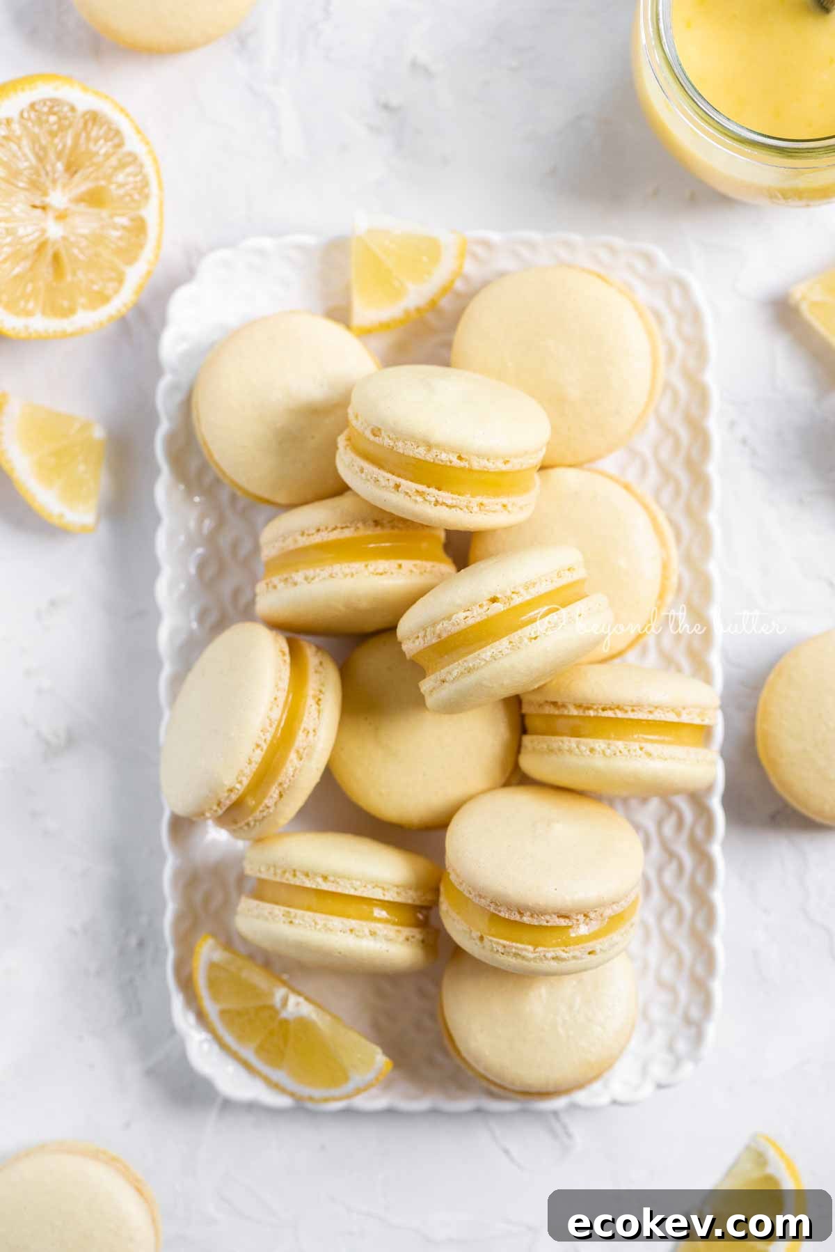 Overhead image of lemon bar macarons on a white dessert tray with lemon wedges | All Images © Beyond the Butter™