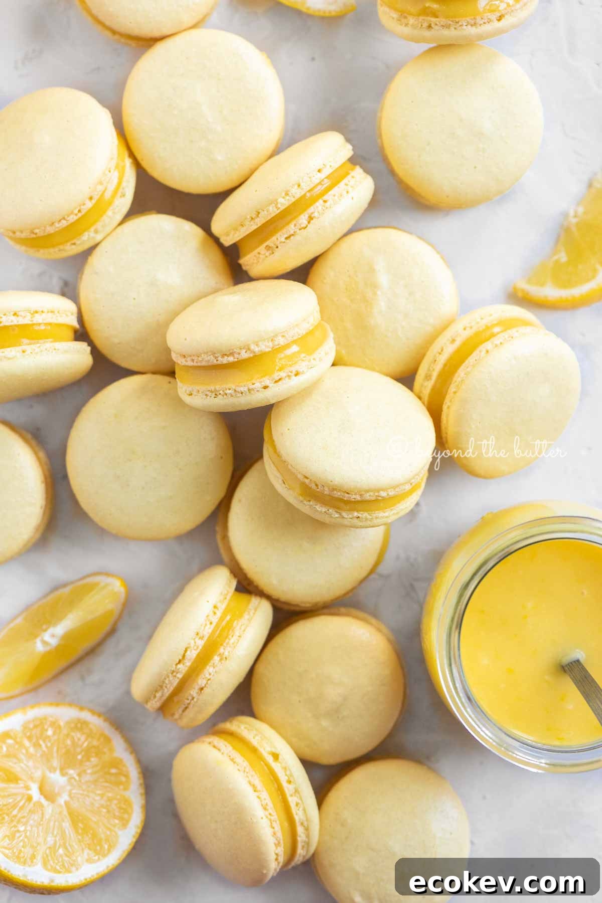 Overhead image of lemon bar macarons randomly placed around a small jar of lemon curd filling | All Images © Beyond the Butter™