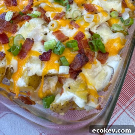 Close up corner of a casserole dish with crispy bacon bits and slices of green onion sprinkled over top of two cheeses melted on a chicken and potato mixture in a glass dish.