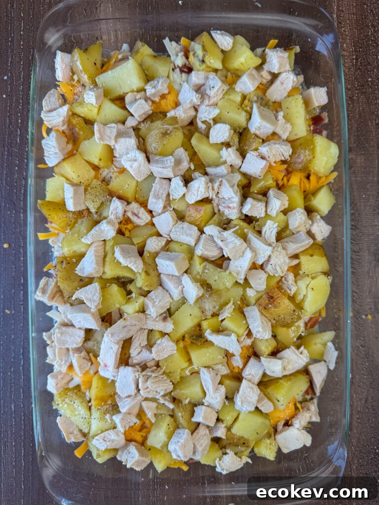 Tender cubes of chicken sprinkled over chunks of Yukon gold baked potatoes in a glass 9 x 13" casserole dish.