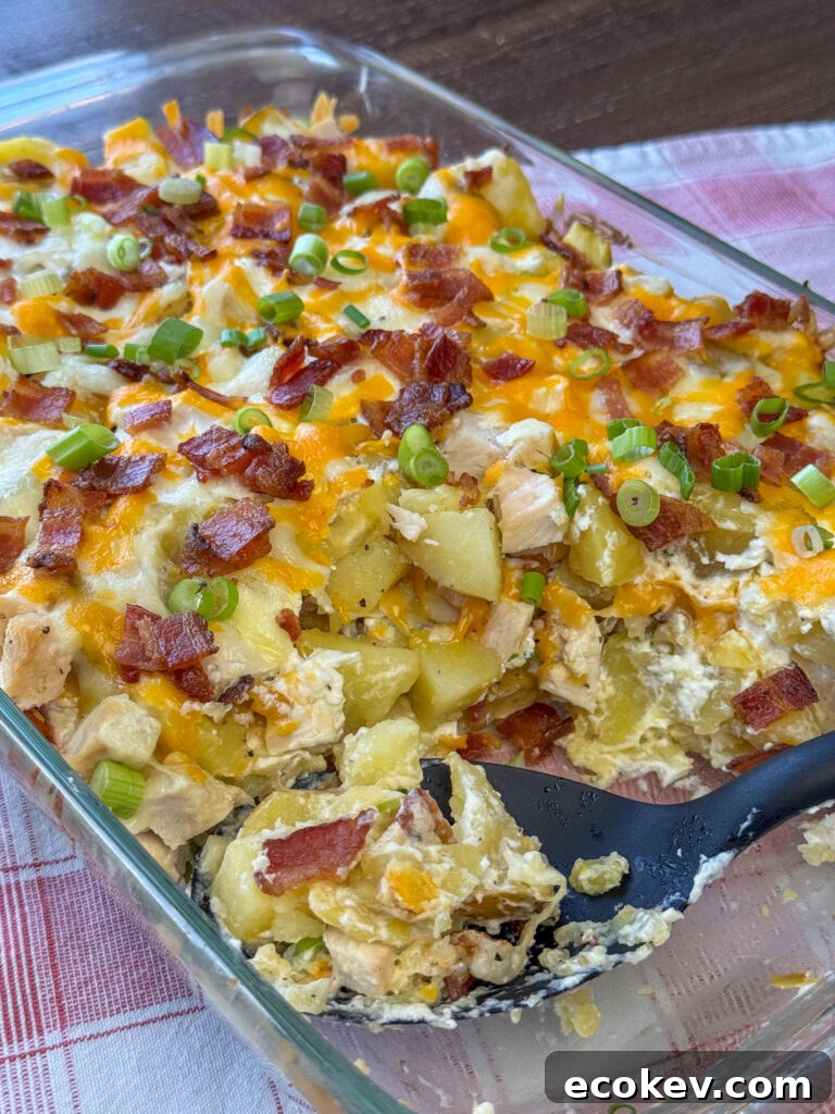 Serving spoon resting in a dish of delicious loaded chicken and potato casserole on a red and white plaid napkin.