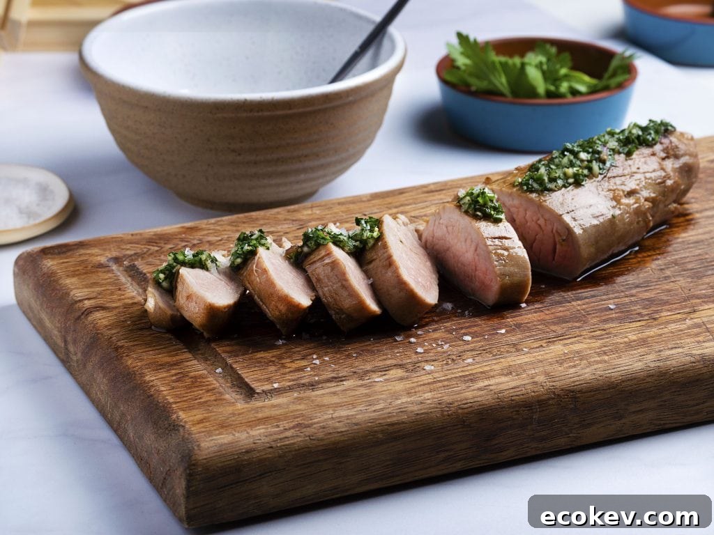 sous vide pork tenderloin sliced on a wooden cutting board with green herb sauce