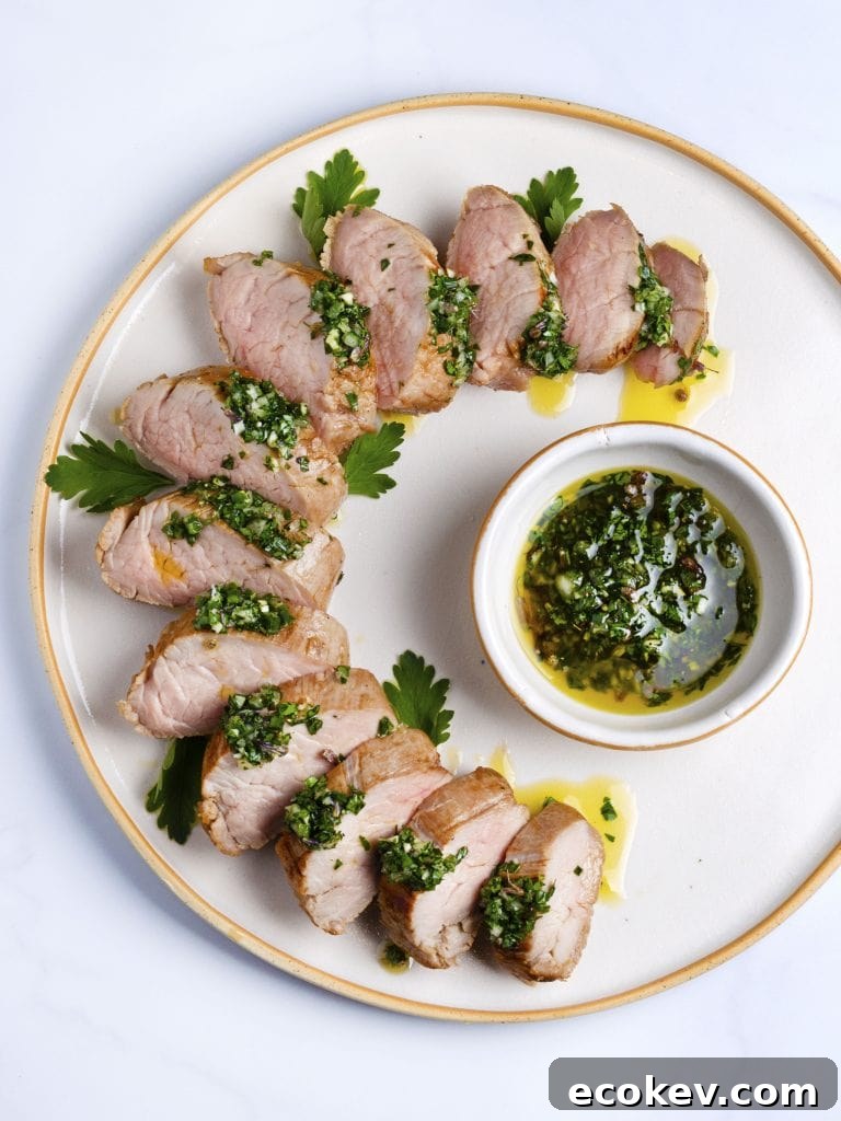 sous vide pork tenderloin sliced on a white platter with green herb sauce