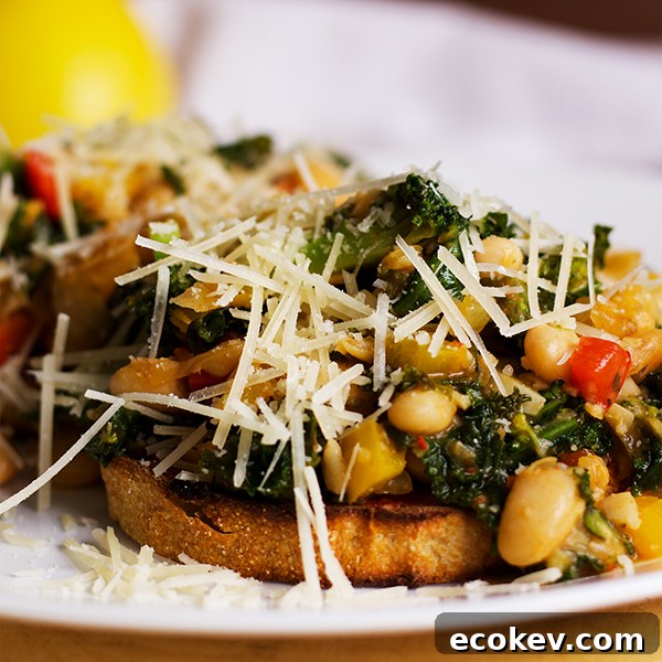 A plate with two slices of toast topped with white beans, veggies and greens, sprinkled with grated parmesan cheese.