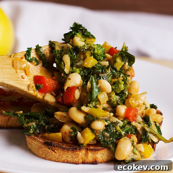 Spoonful of white beans with veggies being served on toast.