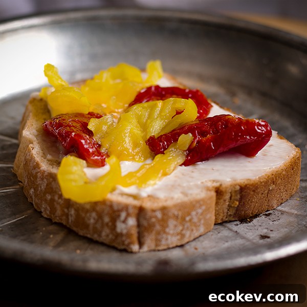 A piece of toast with mayonnaise, banana peppers, and sun dried tomatoes.
