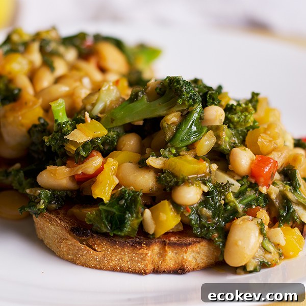 A plate with two slices of toast topped with white beans, veggies and greens.