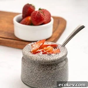 A glass jar filled with chia pudding, topped with sliced strawberries and shredded coconut.