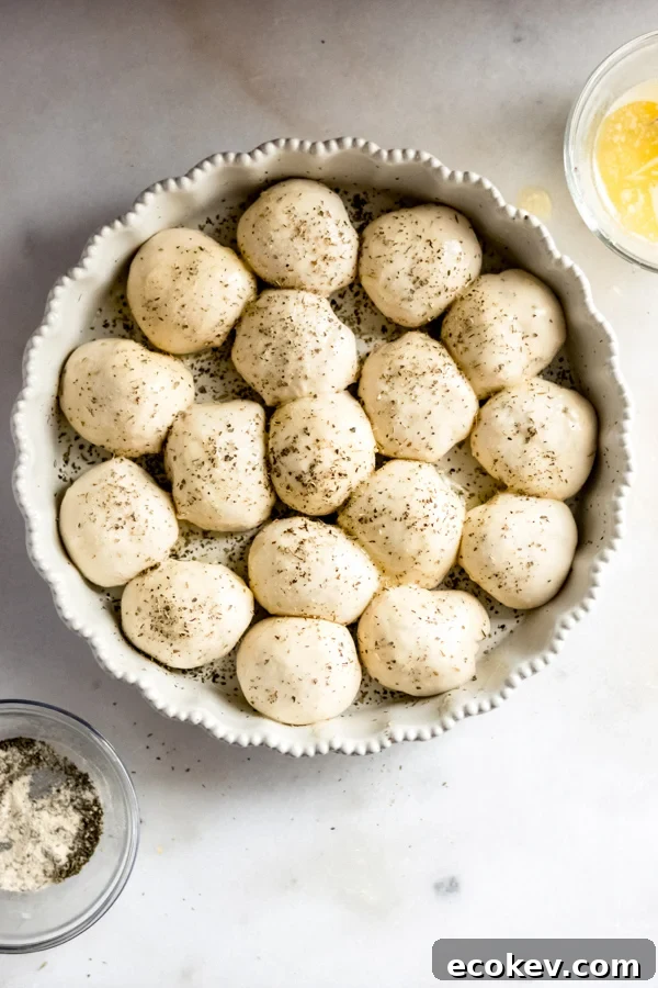 A pan of the rolls brushed with butter and sprinkled with herbs, ready to be baked.