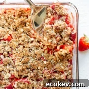 Serving spoon digging into a square glass dish of Strawberry Coconut Crisp.