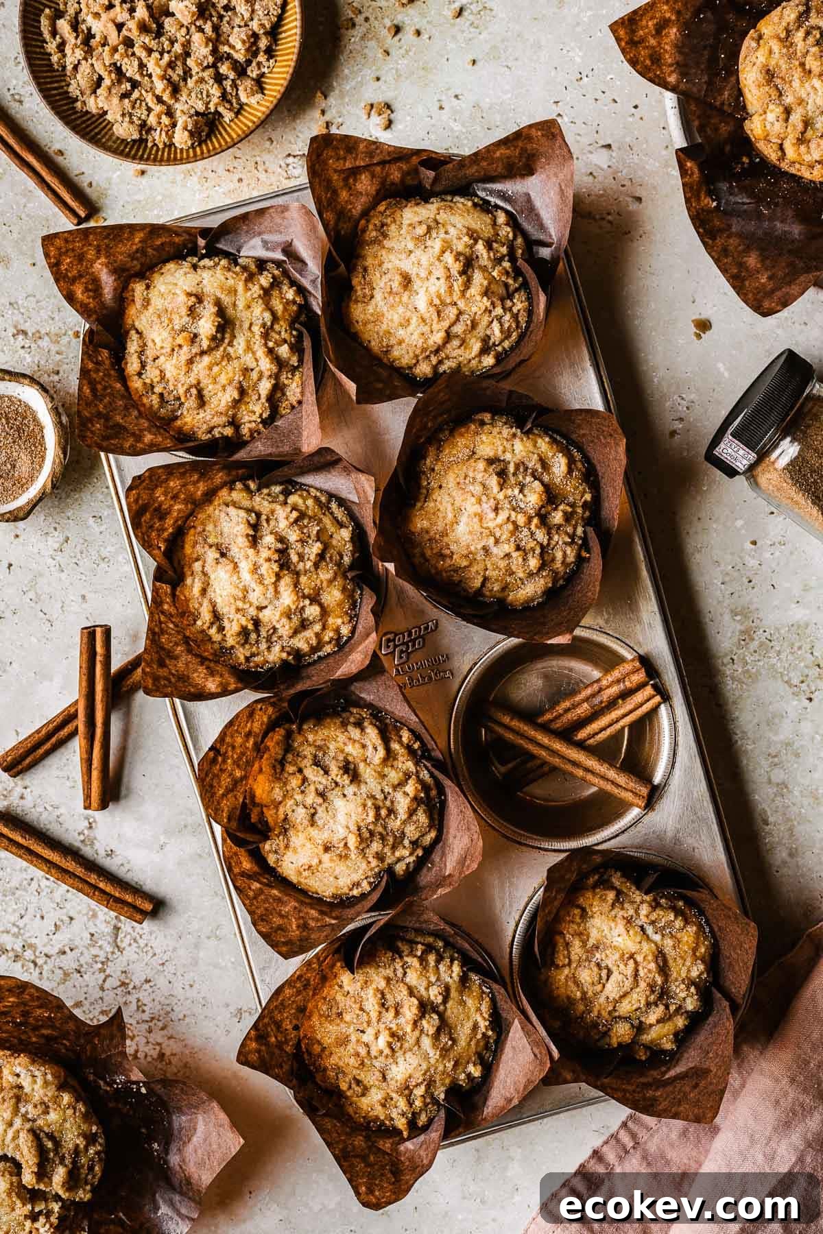 Streusel topped muffins in brown paper parchment liners in a muffin tin.