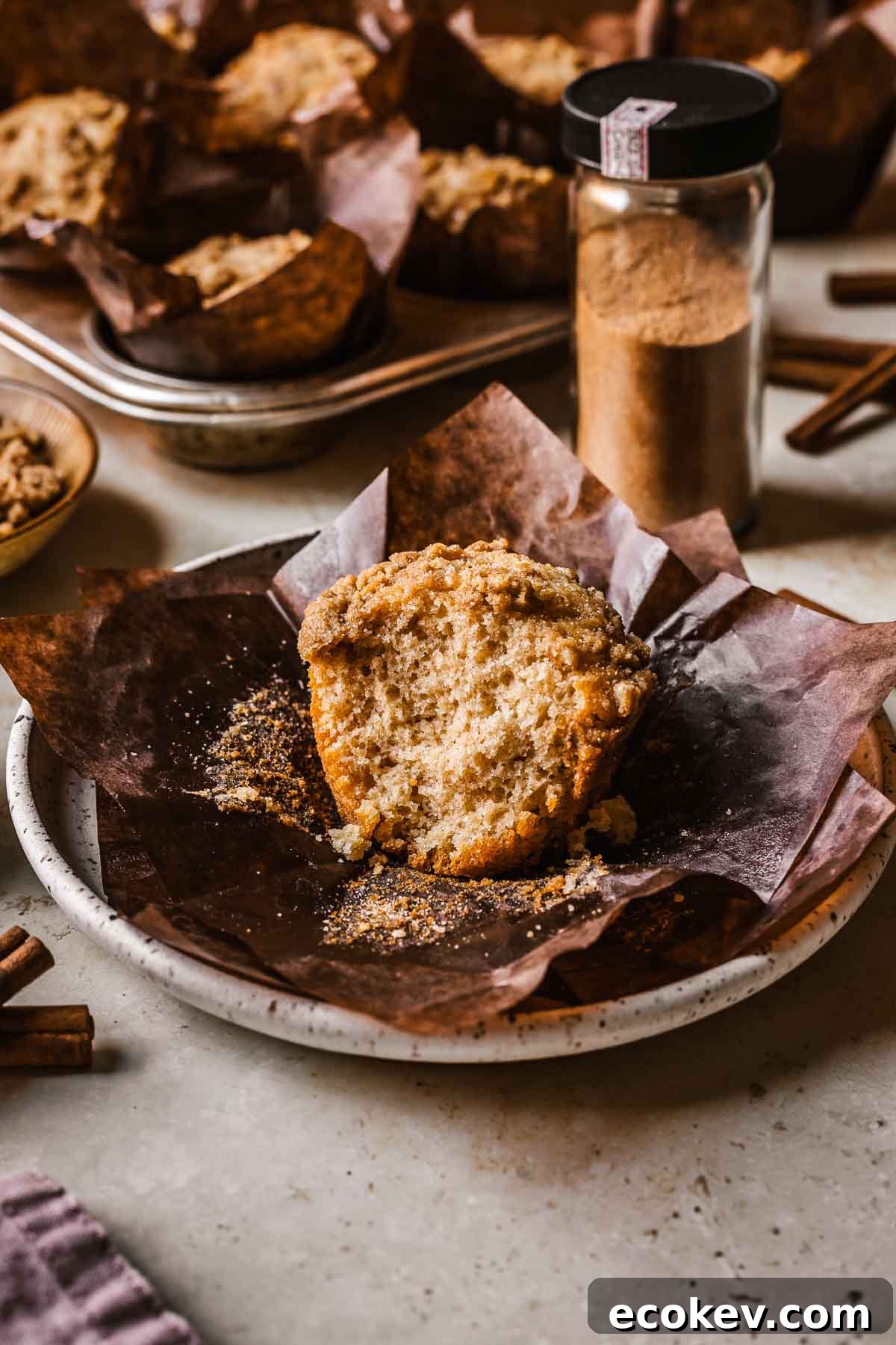 An unwrapped cinnamon streusel muffin on brown parchment on a plate.