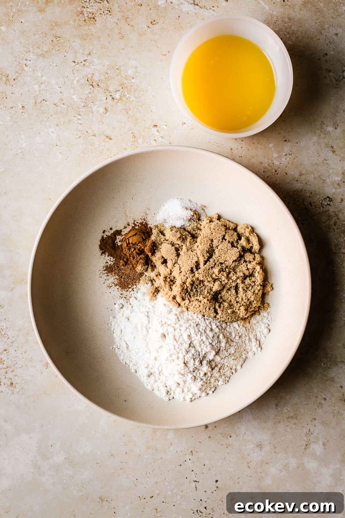A shallow tan bowl filled with dry ingredients and a small bowl of melted butter.