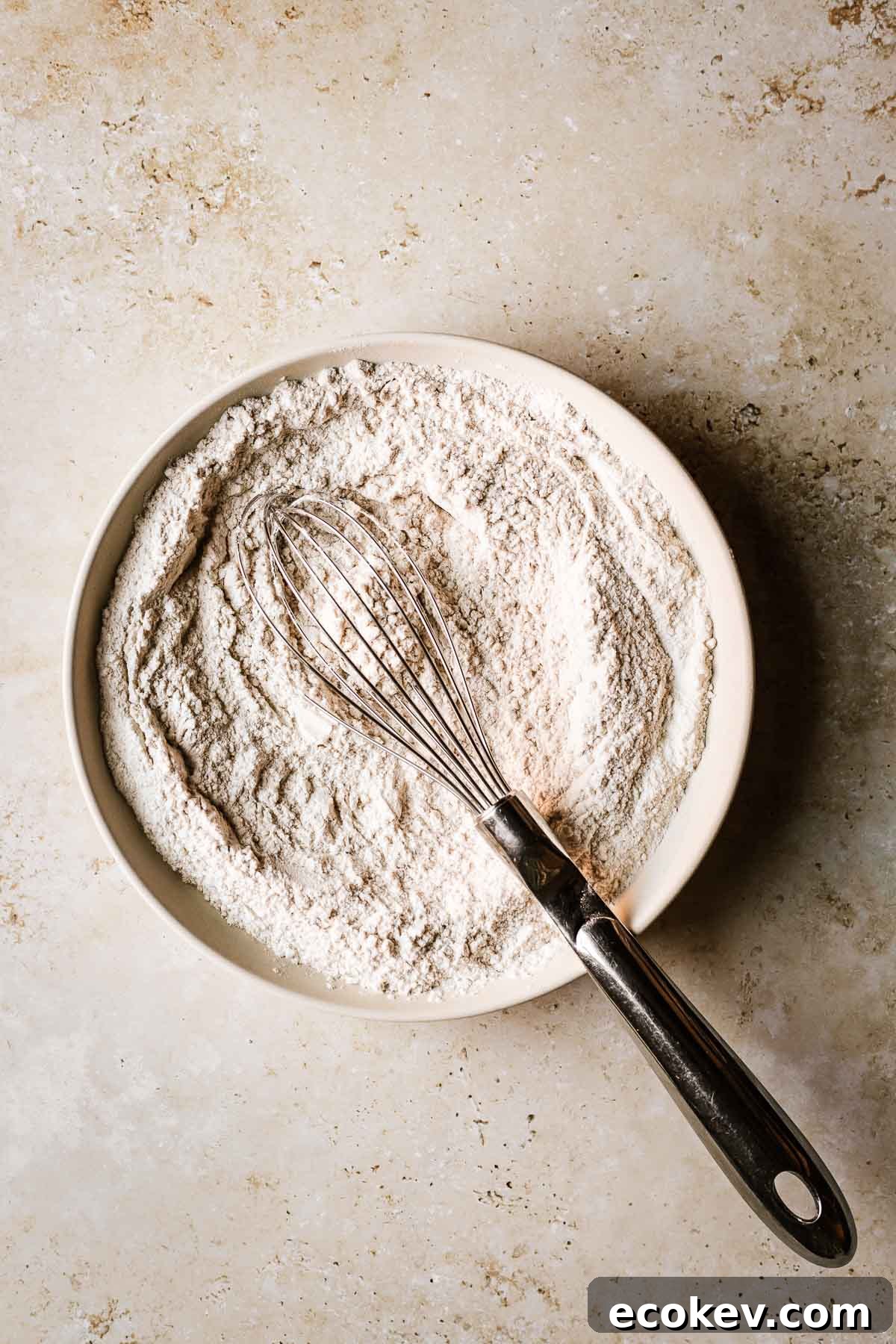 A shallow tan bowl filled with whisked dry ingredients.