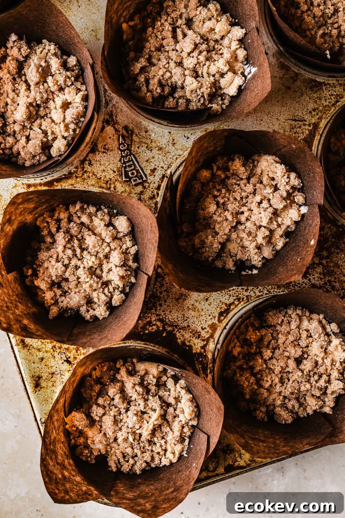 Unbaked muffins covered in streusel topping.