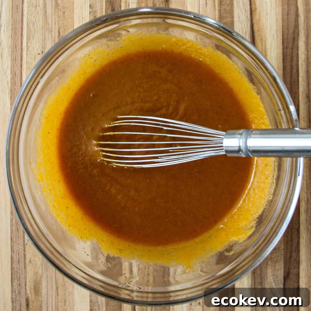 A mixture of oil, pumpkin puree, egg, sugar, and vanilla in a glass bowl with a whisk.