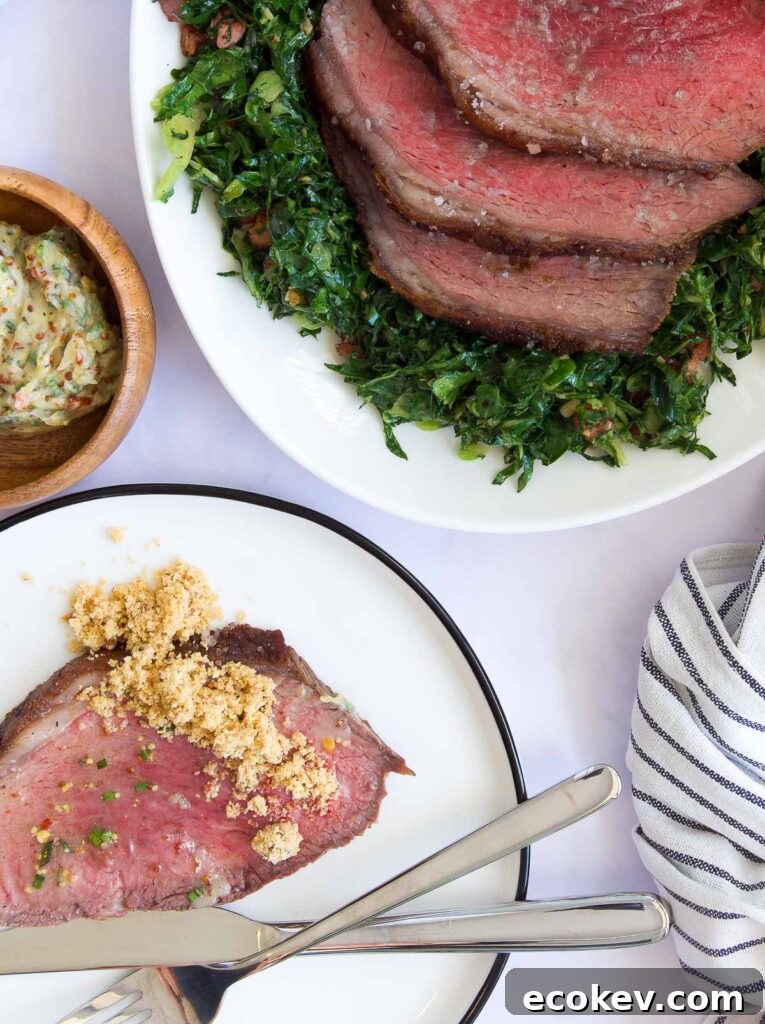 a plate with a slice of Picanha Roast topped with farofa next to a platter with the rest of the roast and greens