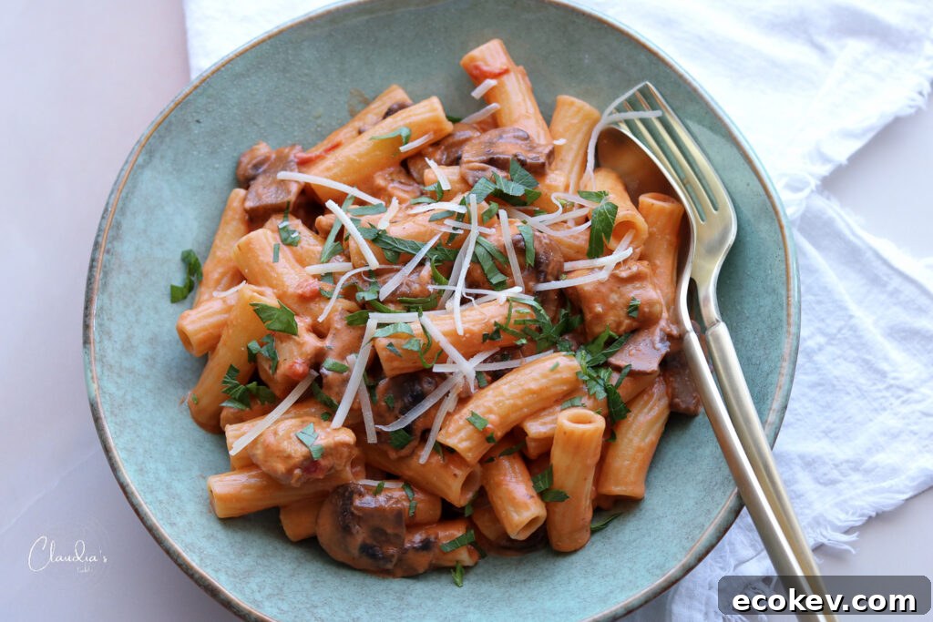 horizontal creamy tomato chicken and mushroom pasta in blue bowl with white napkin