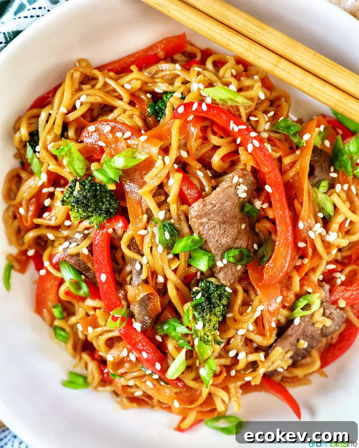 Sesame Garlic Noodles with Steak, broccoli, red peppers, carrots, in a white bowl with chopsticks.