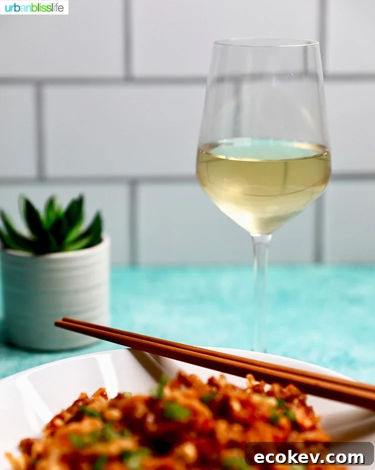 glass of white wine with noodles in a white bowl and chopsticks on the side.