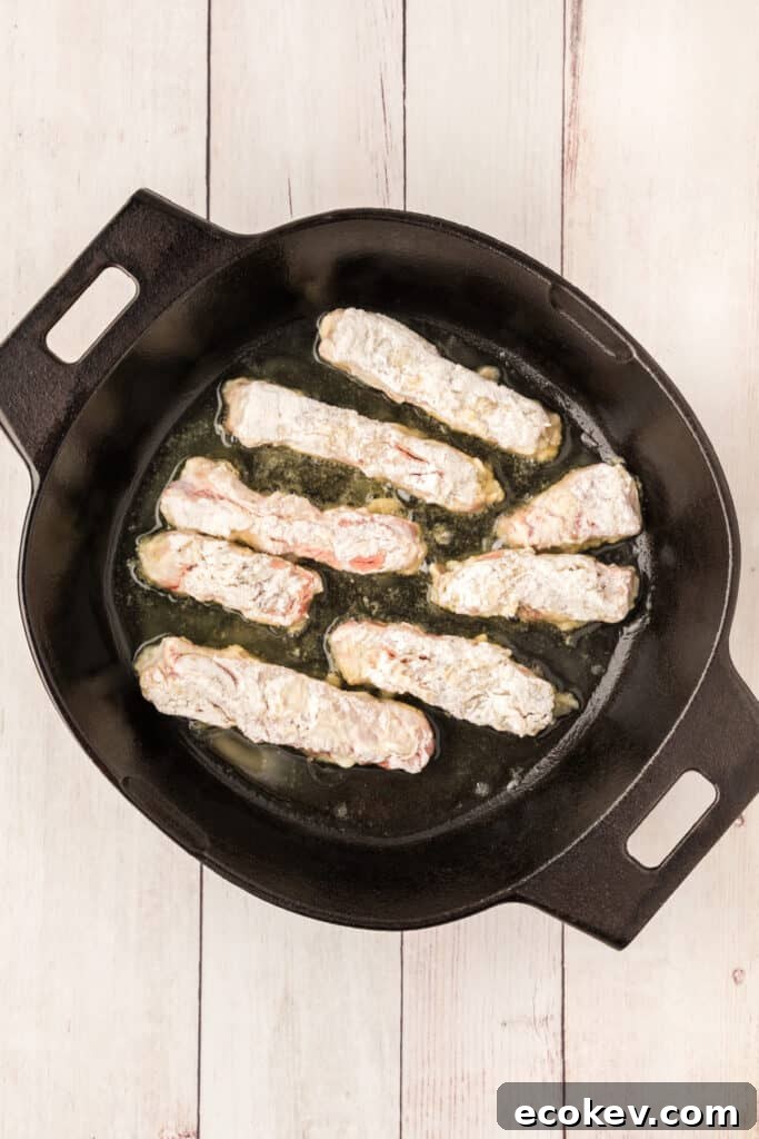 Heat 2 tablespoons of the oil in a skillet over medium heat. Add half of the strips and brown on both sides. 