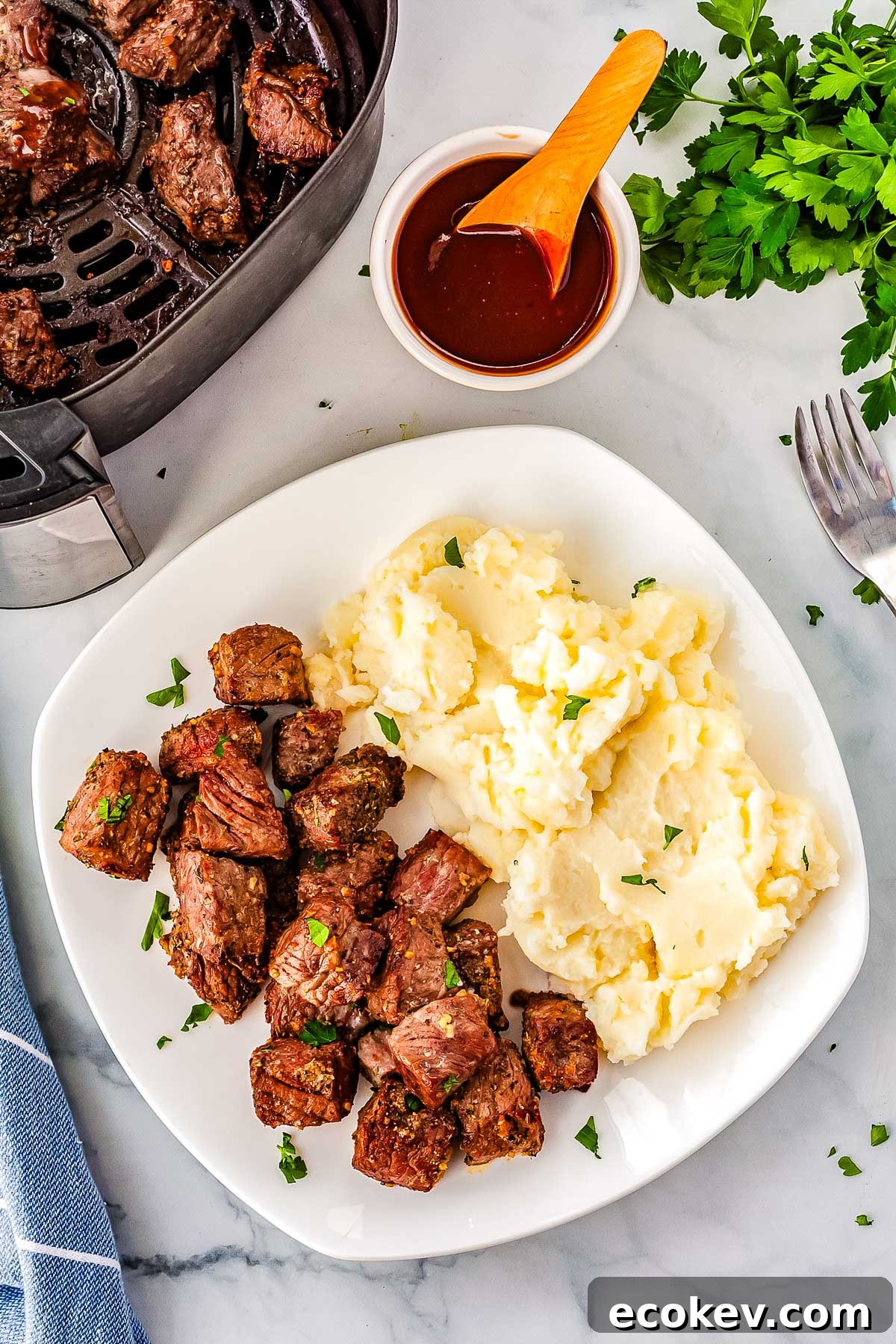 The finished steak bites on a white plate with mashed potatoes.