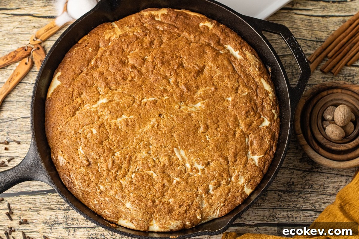 A cast iron skillet filled with a golden pumpkin cookie swirled with creamy cheesecake, baked until soft