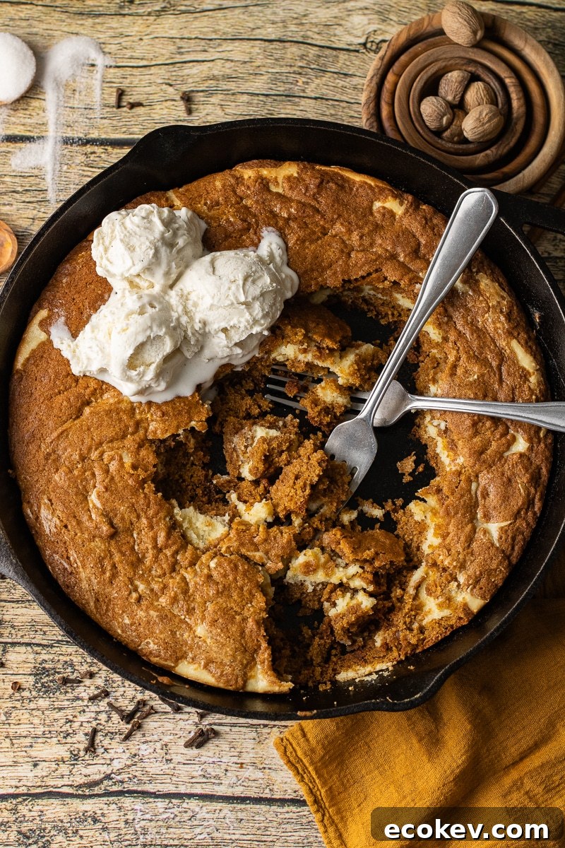 A cast iron skillet filled with a golden pumpkin cookie swirled with creamy cheesecake, baked until soft in the center with crisp edges
