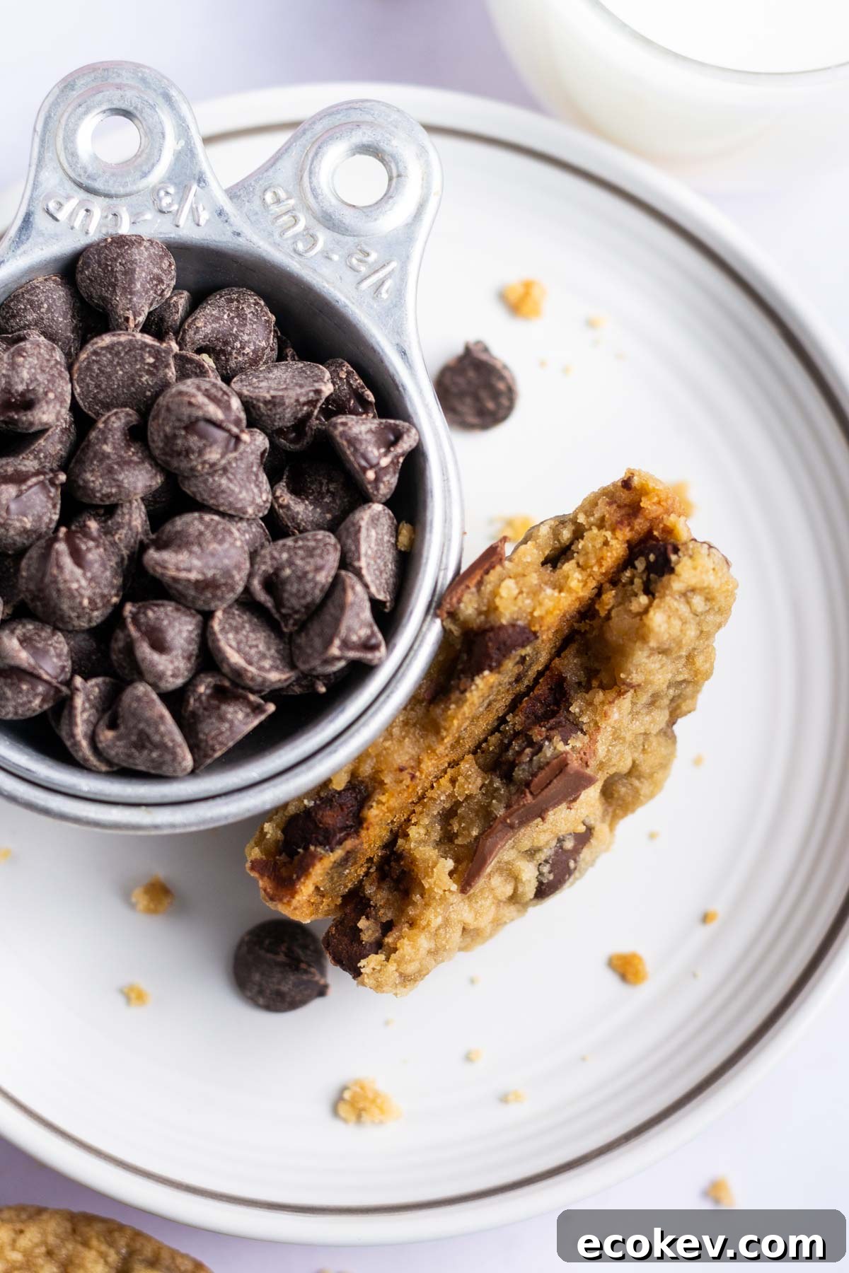 broken chocolate chip cookie with a cup of chocolate chips on a plate