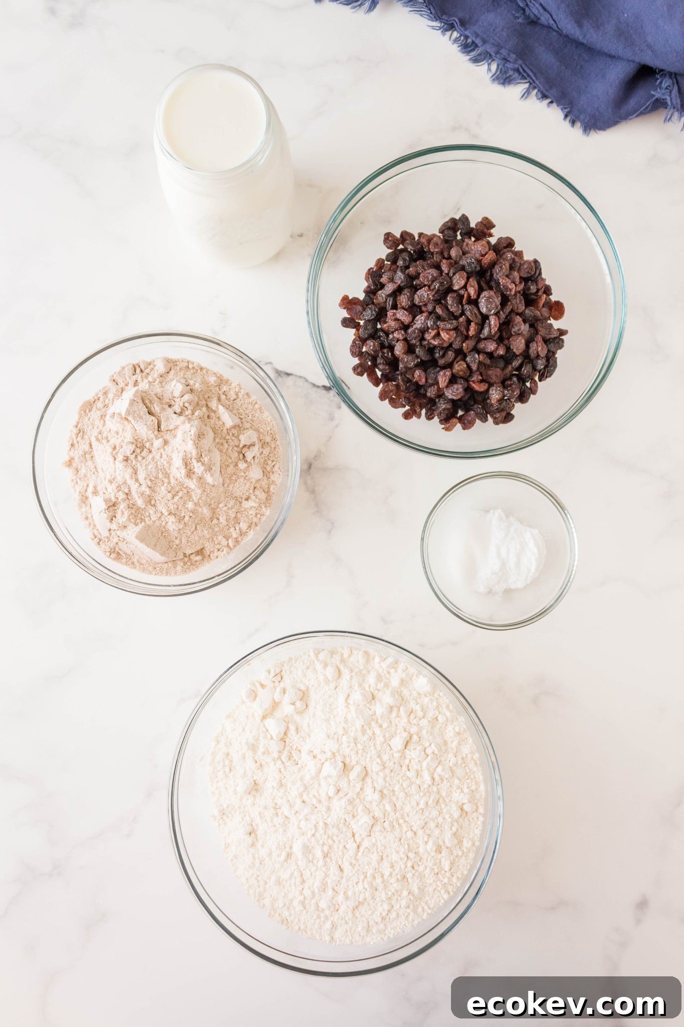 Ingredients used to make Irish Soda Bread including flour, baking soda, buttermilk, raisins and salt.