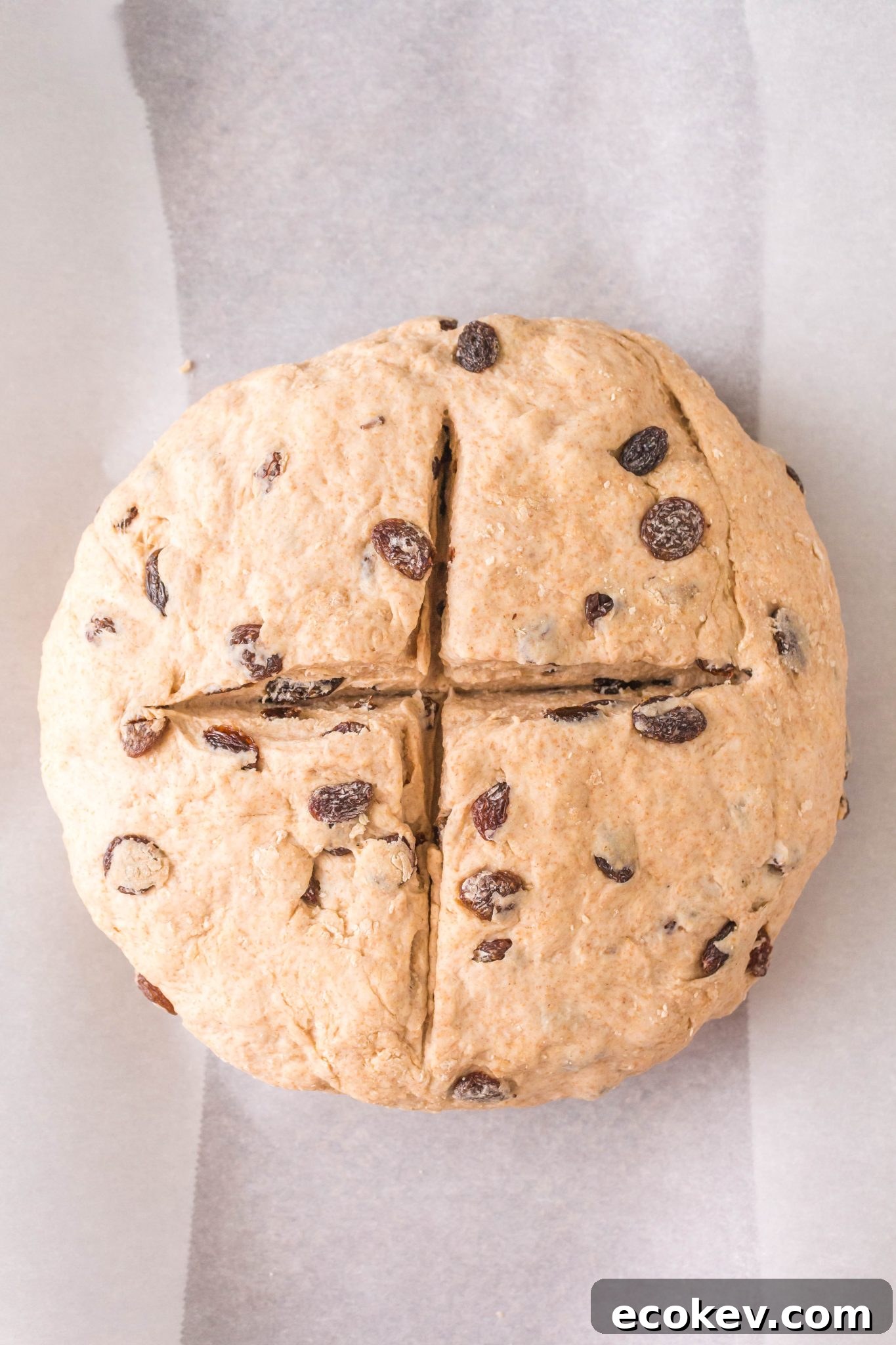 Top down view of a shaped loaf of soda bread with a cross cut into the top.