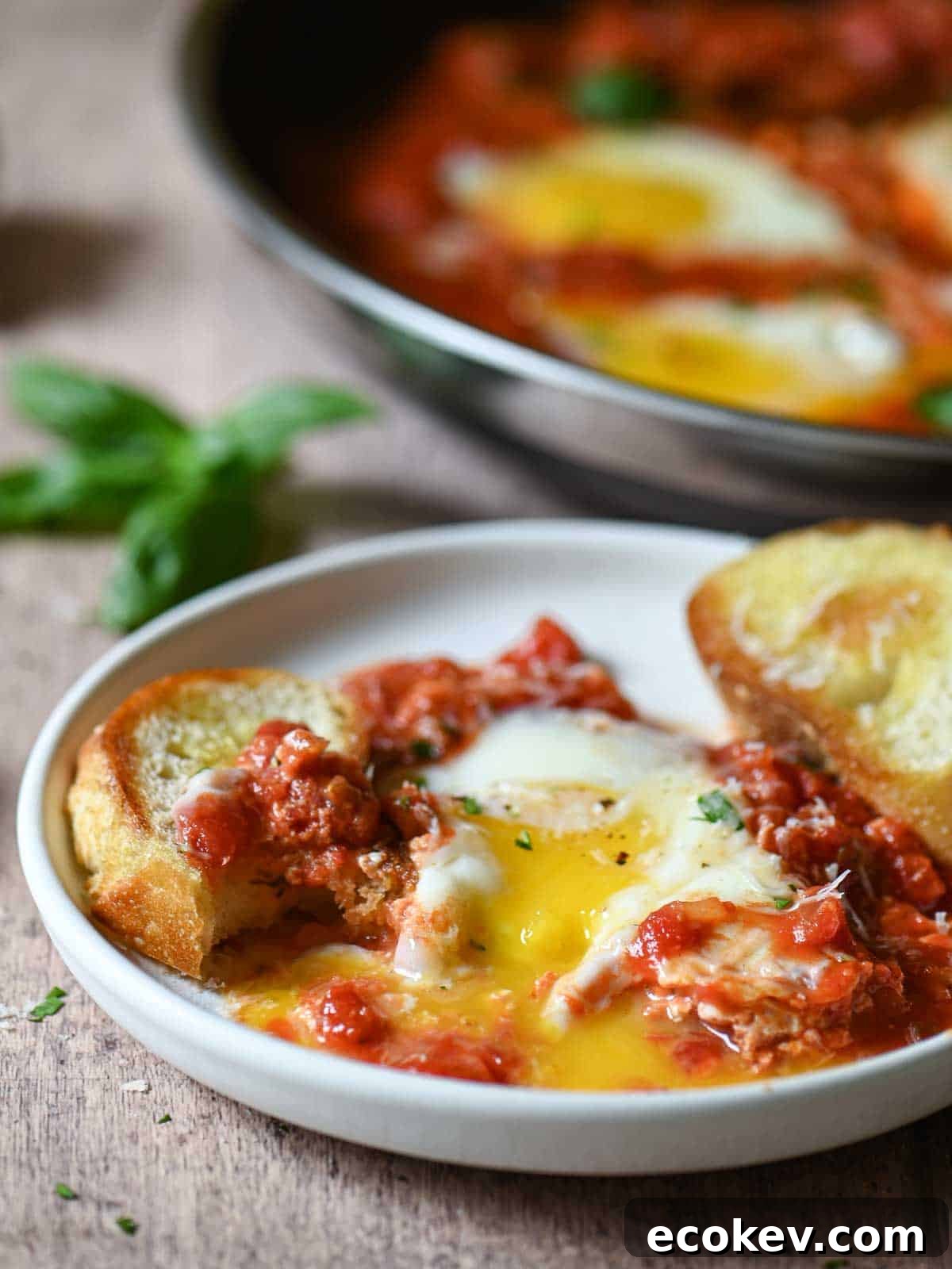 Savory eggs in tomato sauce with garlic bread on a white plate, fresh basil garnish.