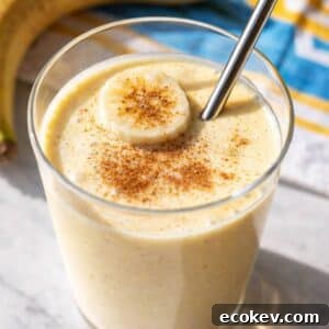 Greek Yogurt Banana Smoothie in tall glass with sliced banana on marble table.