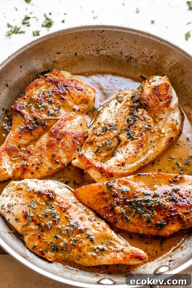 four chicken breasts cooking in a stainless steel skillet