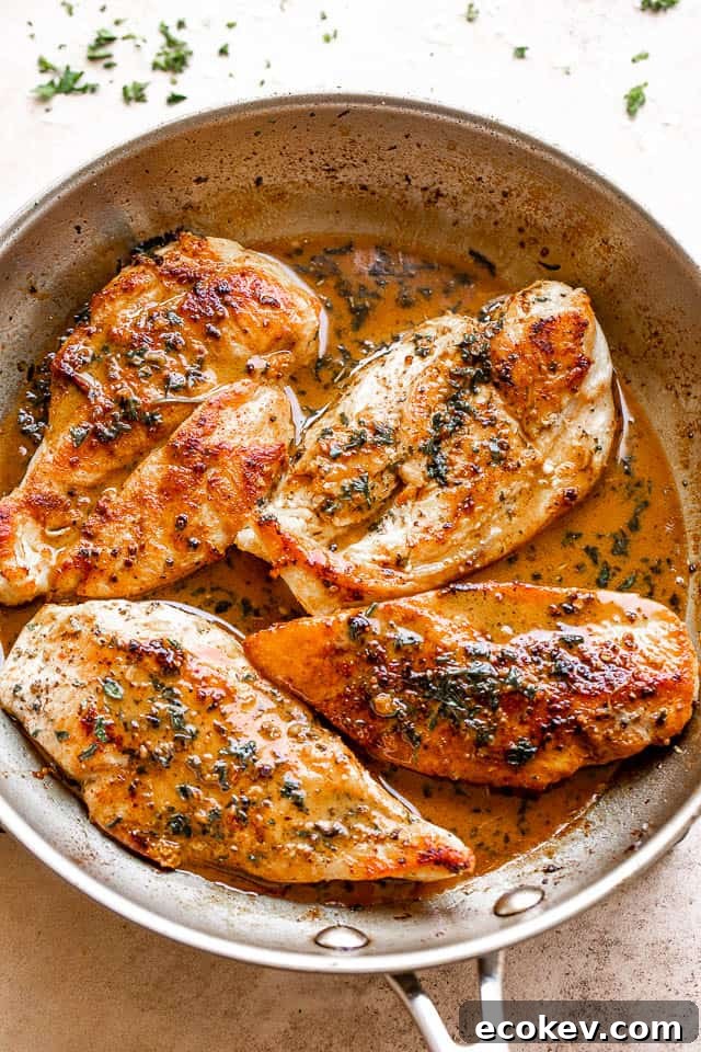 four chicken breasts cooking in a stainless steel skillet
