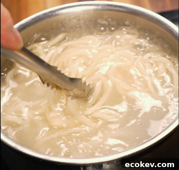 Authentic Dan Dan Noodles with Spicy Sichuan Sauce 4 Noodles boiling in a pot of water being stirred with tongs — prepping the base for dan dan noodles.