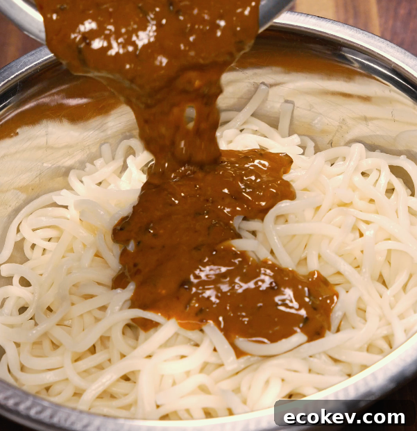 Authentic Dan Dan Noodles with Spicy Sichuan Sauce 6 Spicy dan dan sauce being poured over cooked noodles in a metal bowl — ready to toss and serve.