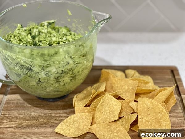 Green Goddess Salad in a glass bowl on a Wood cutting board wit some chips next to it.