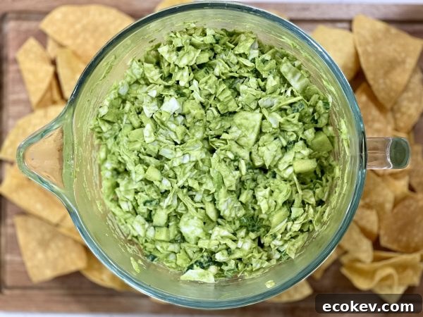 Green Goddess Salad in a glass bowl on a Wood cutting board wit some chips next to it.