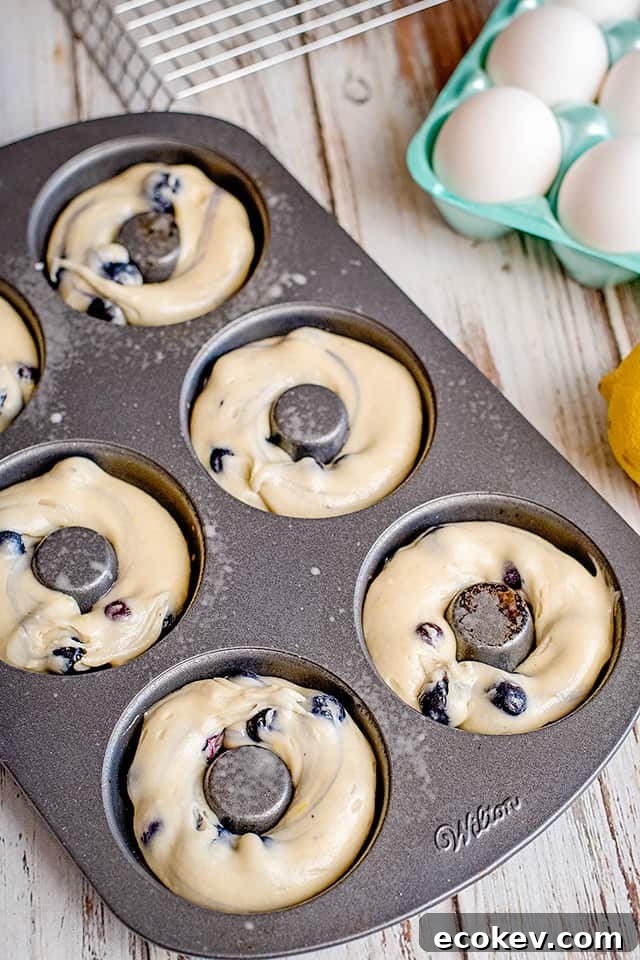 donut pan with donut batter piped in each cavity and eggs beside pan
