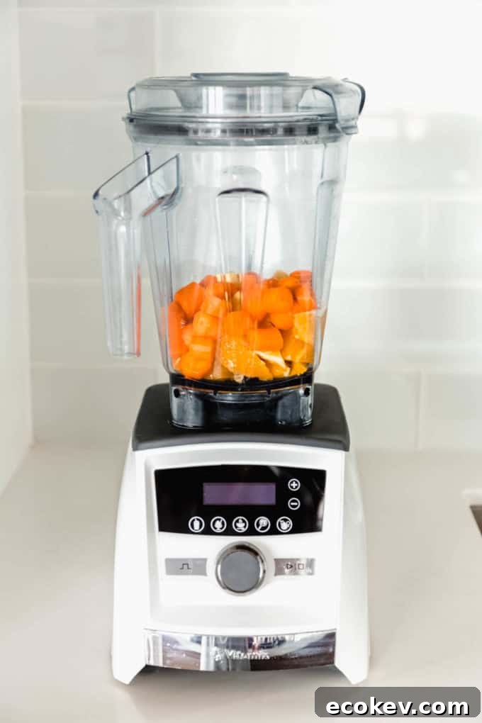 A blender with cut up oranges, carrots and ginger in it