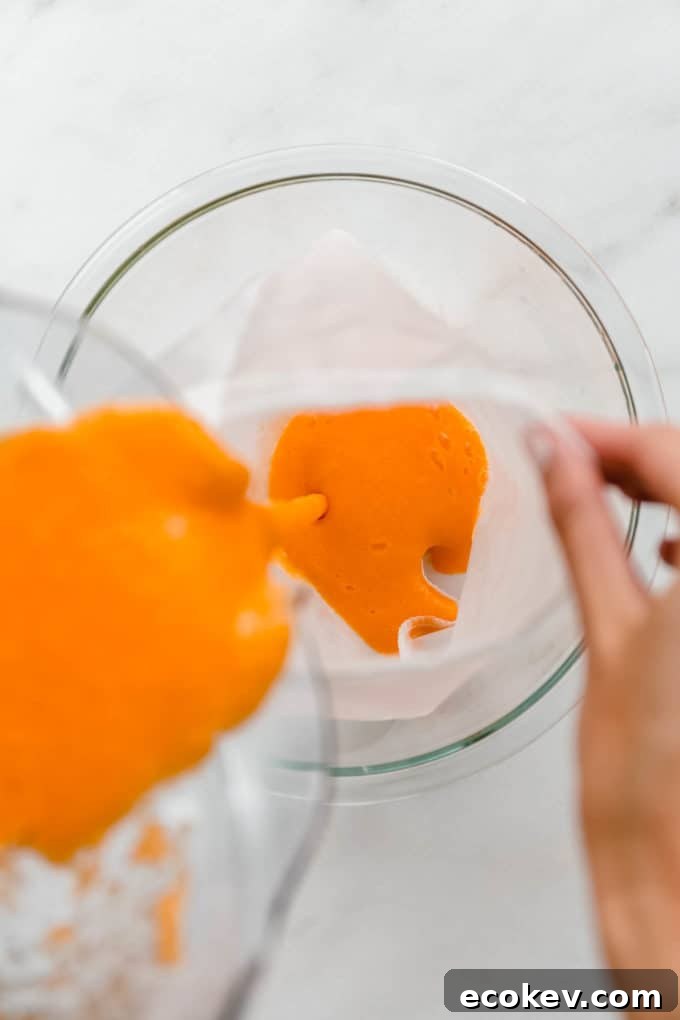 A blender pouring orange, carrot and ginger juice into a mesh straining bag
