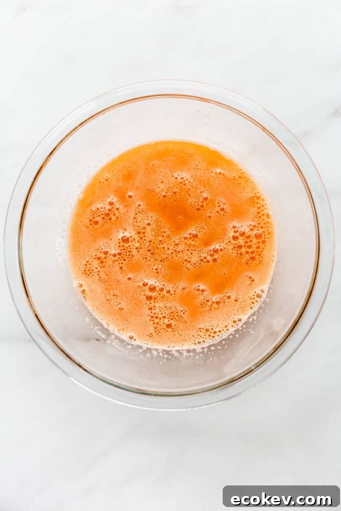 A clear mixing bowl with orange, carrot and ginger juice in it