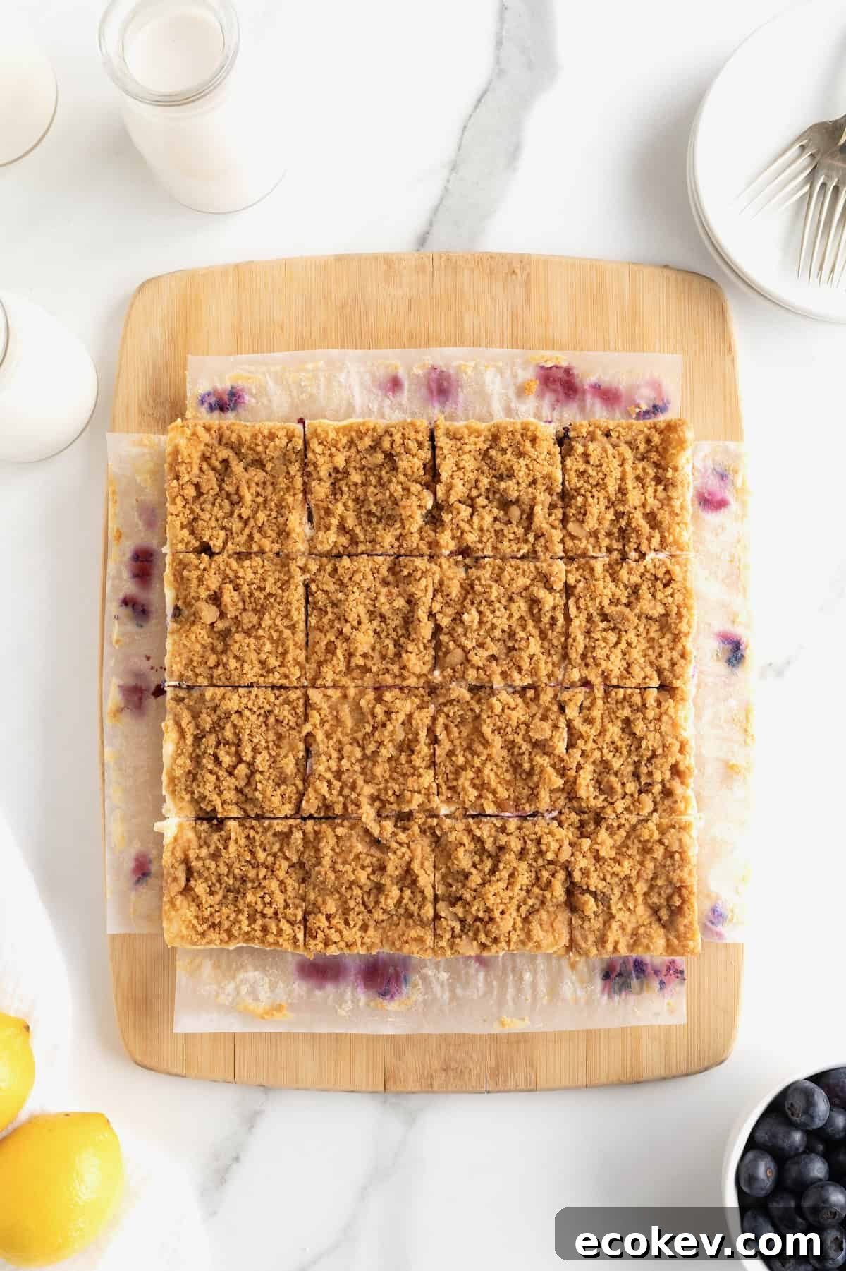 Lemon blueberry cheesecake bars cut into 12 squares on a parchment lined cutting board.