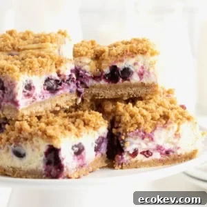 Four lemon blueberry cheesecake bars on a white cake stand.