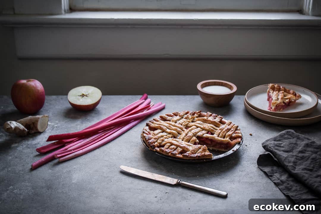 backlit image of baked rhubarb apple pie with ginger and lemongrass next to a window with a slice cut out on a plate nearby along with the pie ingredients