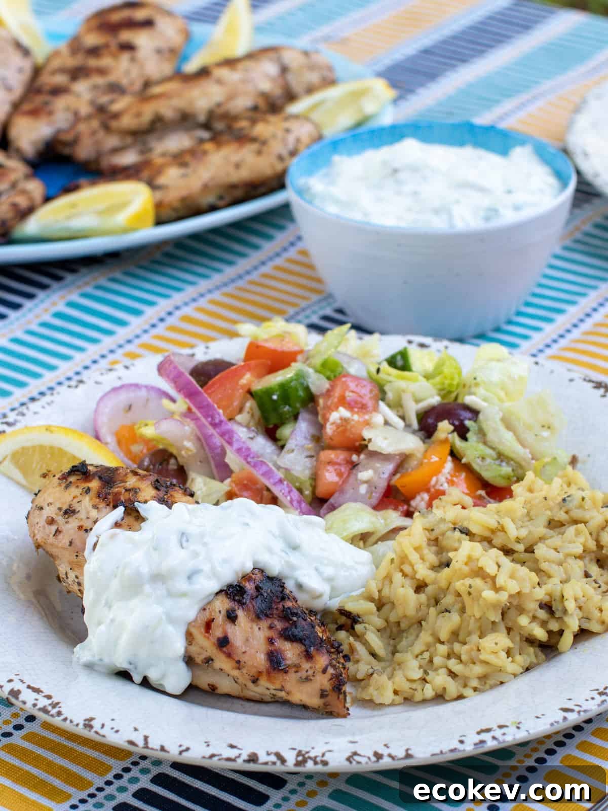 A plate of Greek food including chicken, salad, rice and tzatziki