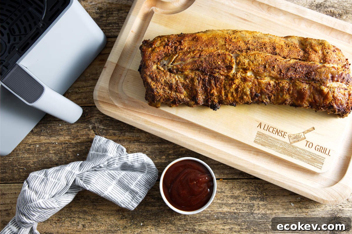Slab of pork ribs on cutting board with air fryer basket and bowl of BBQ sauce.